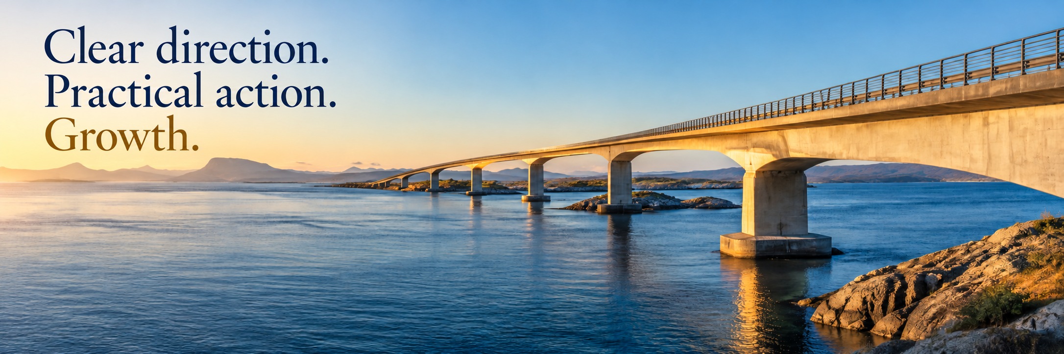A sunlit bridge stretching across blue water towards distant mountains